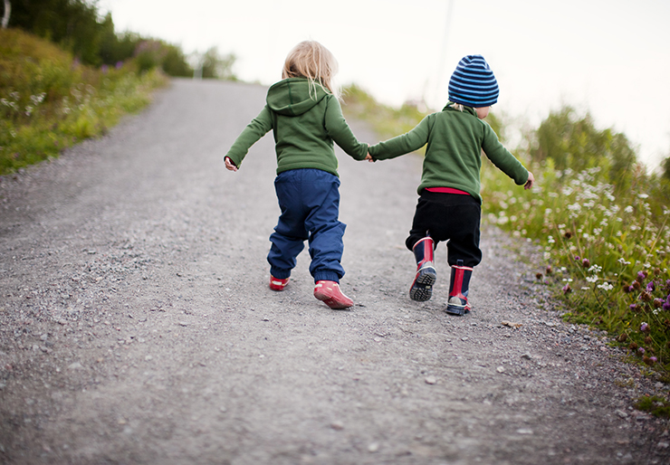Two small kids holding hands while running outdoor.